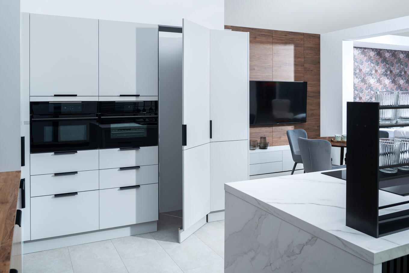 Decodom biela kuchyňa na mieru s modernými zabudovanými spotrebičmi a čiernymi detailmi.