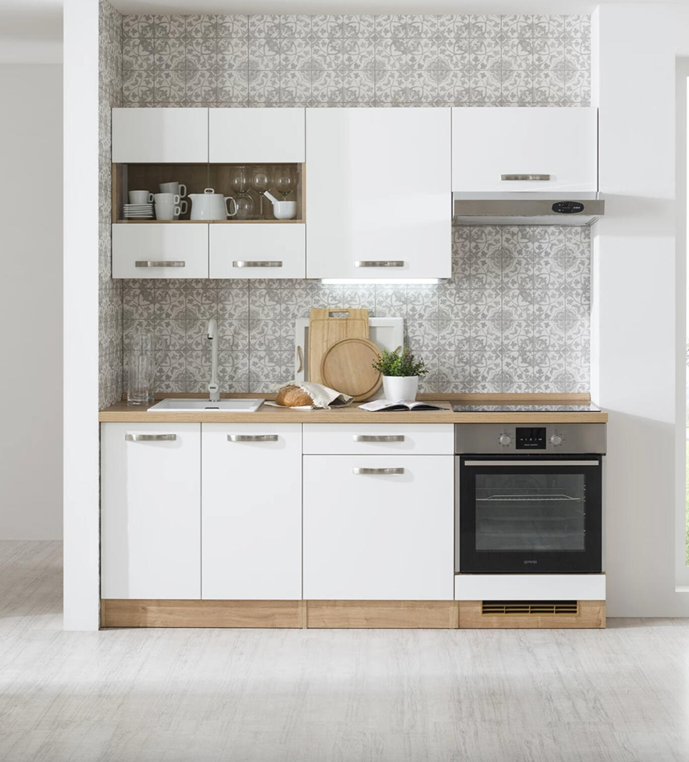 Minimalistická biela kuchyňa s drevenými detailmi a vzorovaným dlaždicovým obkladom.
