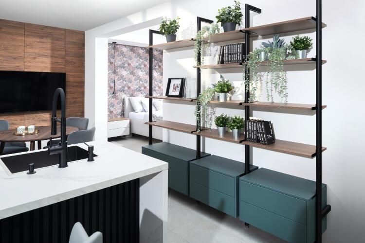 Dizajnová Decodom regálová stena s prirodzeným drevom a zelenými akcentmi, pridávajúca teplú a živú atmosféru do moderného domova. Decodom prispôsobené regály s zelenými rastlinami a trendovým tmavozeleným úložným nábytkom.